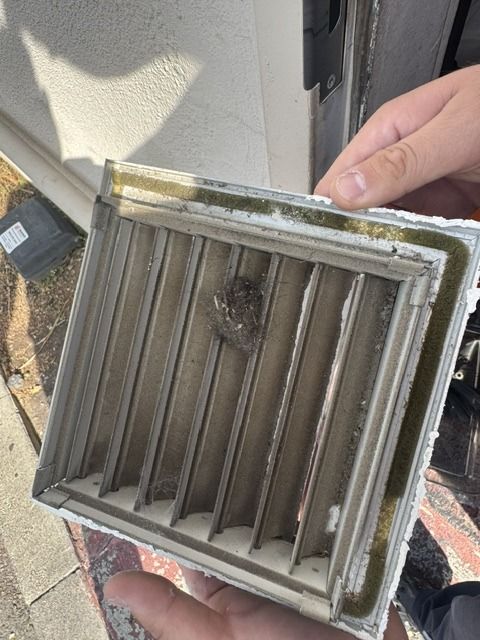 Supply register cover held up to show a thick layer of grey dust on the louvers before cleaning