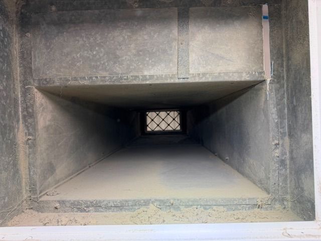 Inside of a rectangular sheet-metal supply duct after cleaning, with the grille visible at the far end
