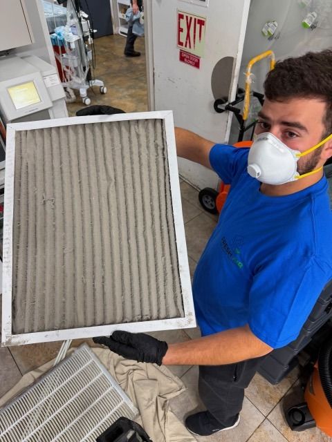 Technician in a respirator holding up a pleated return filter loaded with grey dust